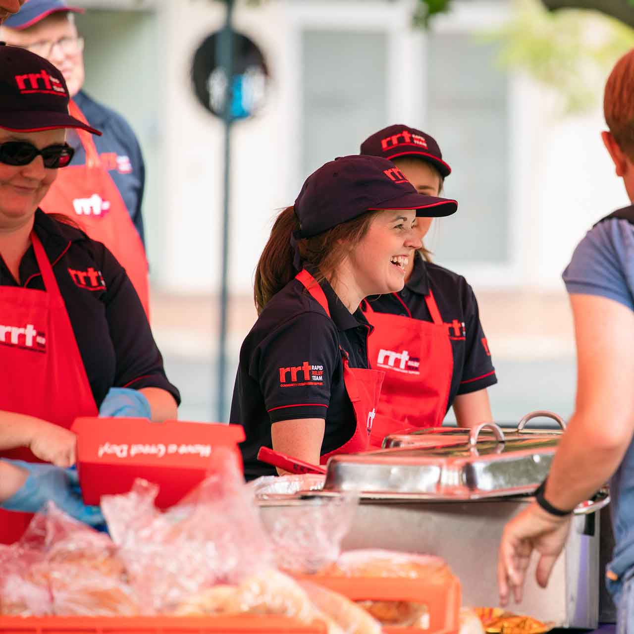 Workers in black and red uniforms serving food. The main worker is smiling away from the camera